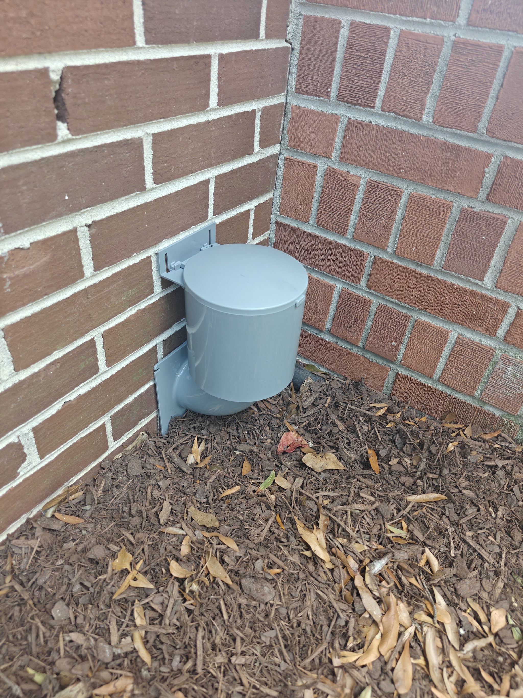 A dryer vent hood fixed to a brick wall above mulch